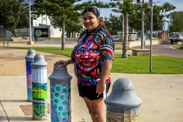Tahira Kelly standing on the street with one of her Fairy Floss Turtle bollards around Geraldton.